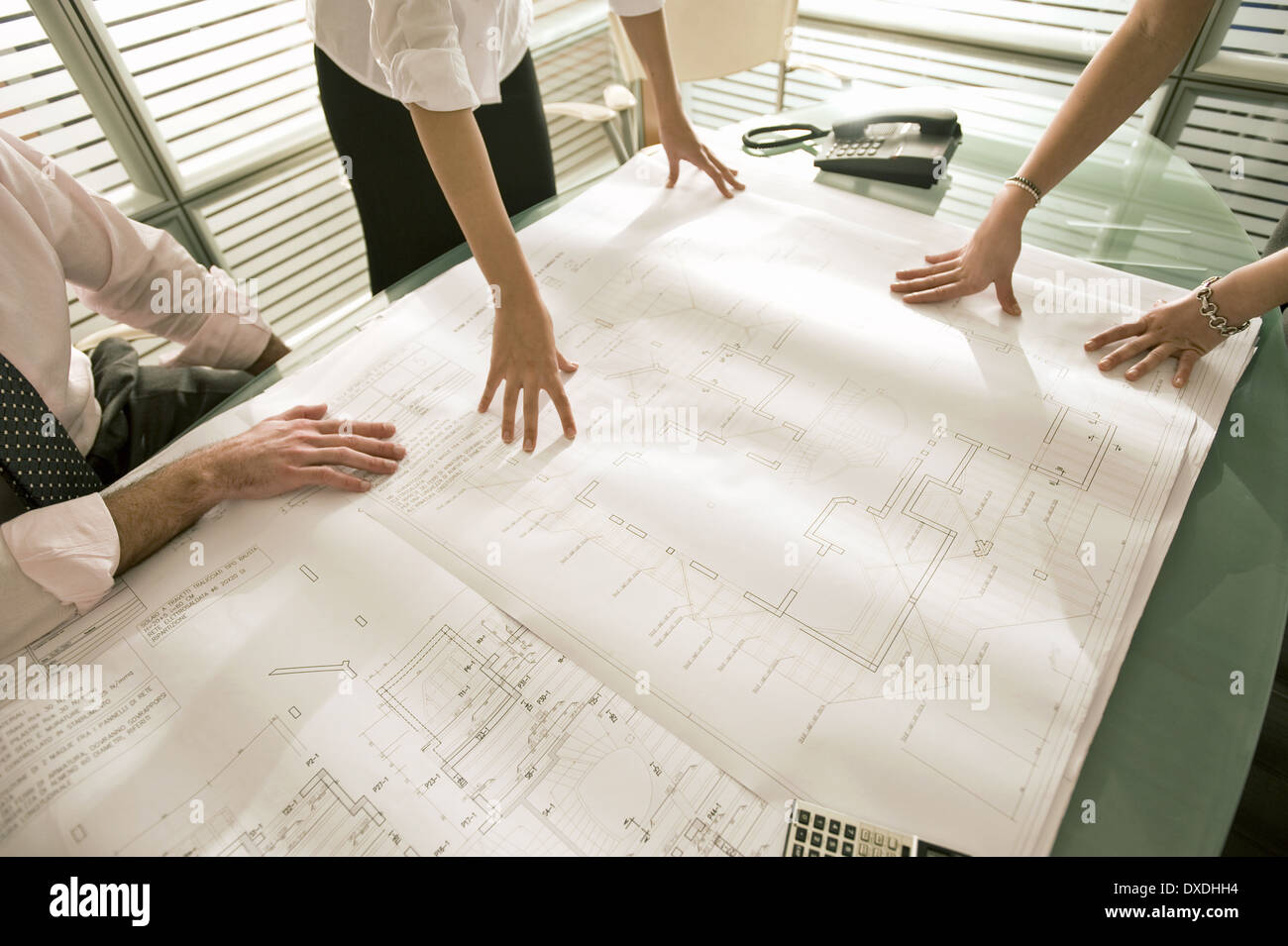 Closeup of professionals looking at architectural plans on desk Stock Photo