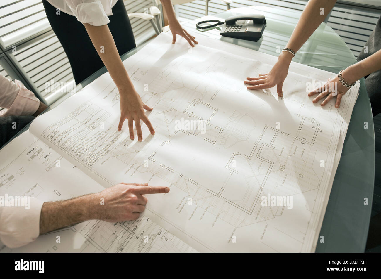 Closeup of professionals looking at architectural plans on desk Stock Photo