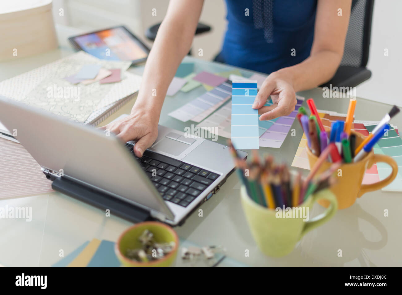 Woman holding color swatches and using laptop Stock Photo