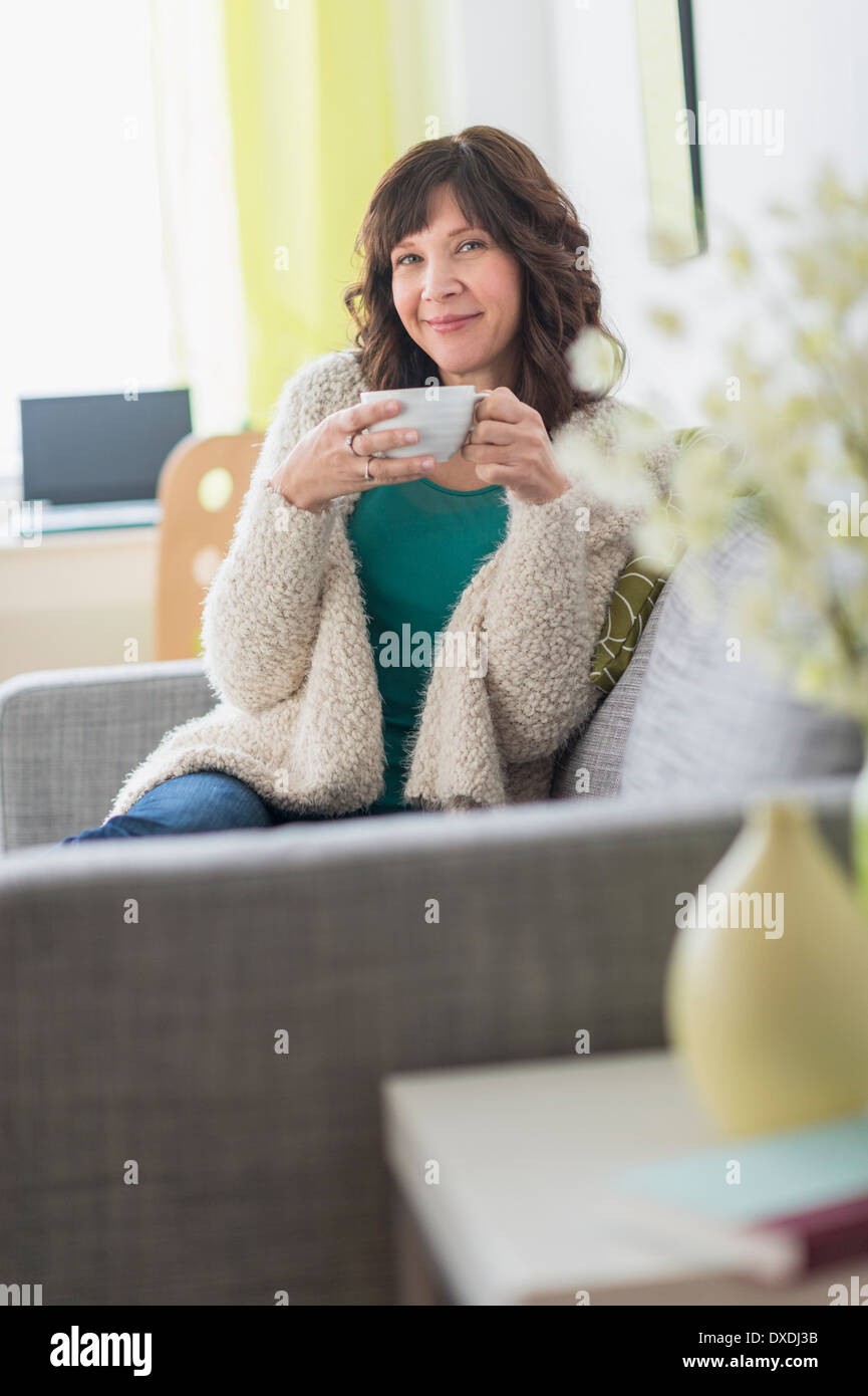 Portrait of woman sitting on sofa holding hot drink Stock Photo - Alamy