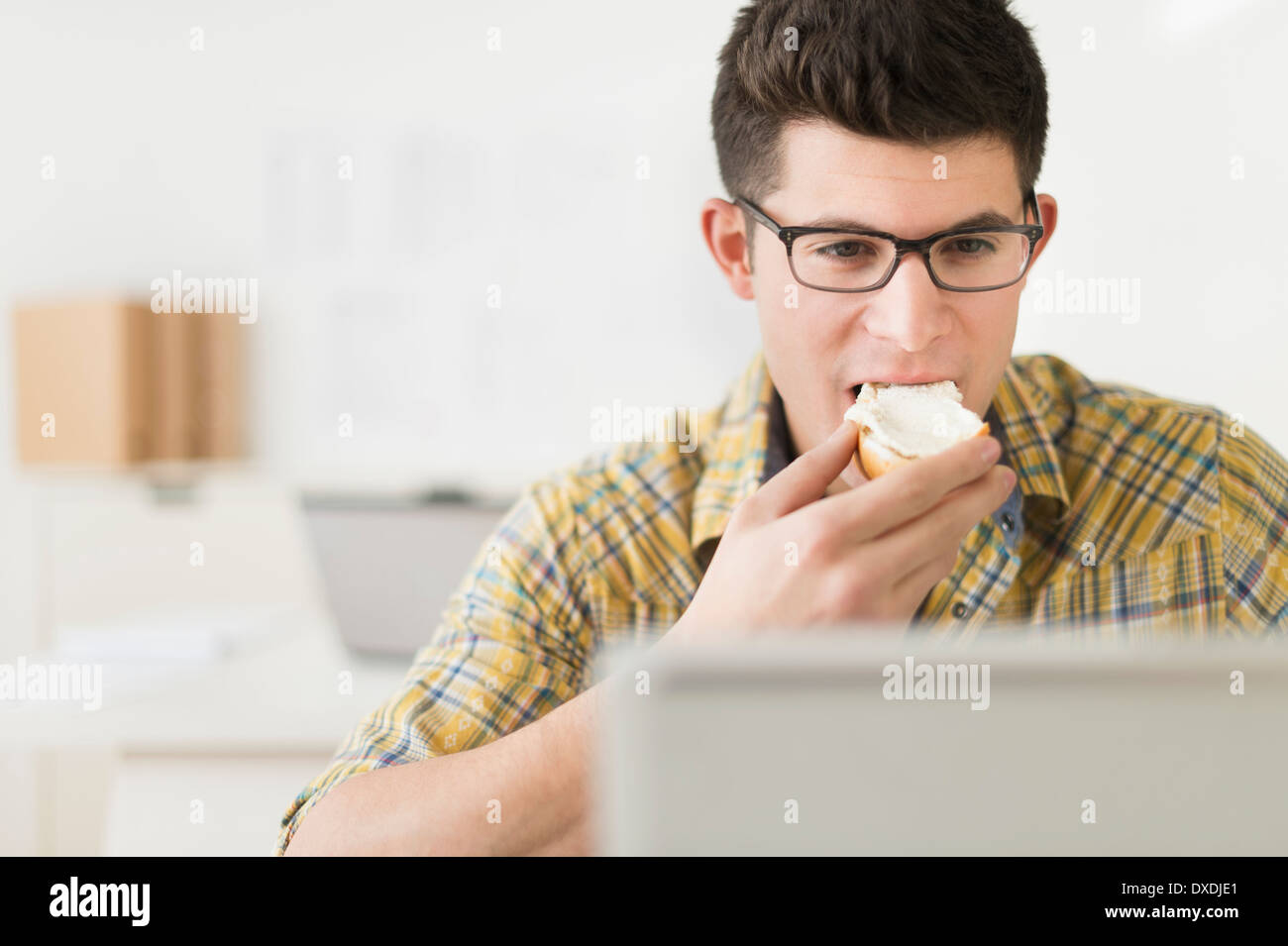 Young man eating sandwich and using laptop Stock Photo
