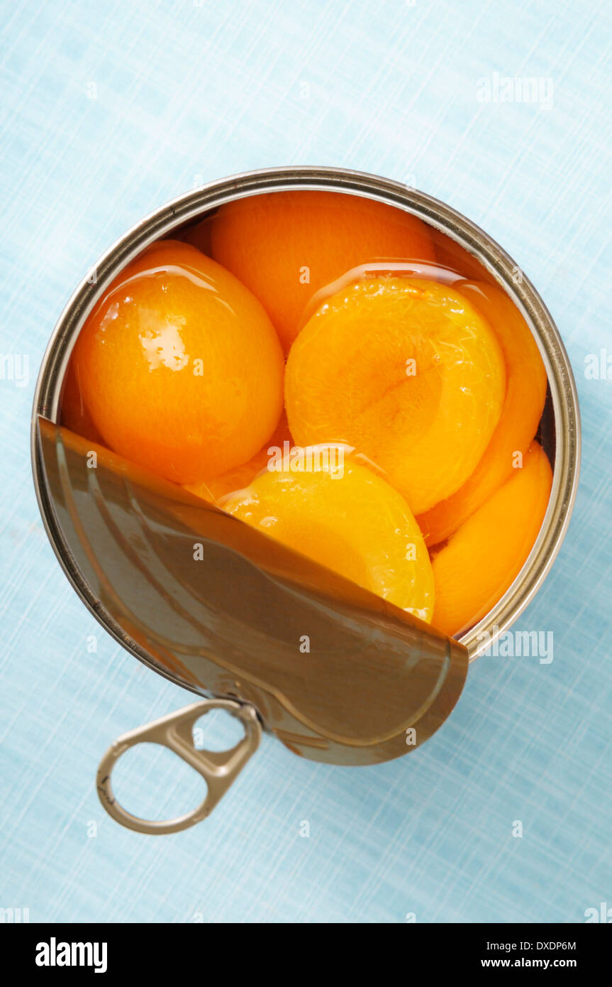 Open can of apricots, on blue background, studio shot Stock Photo