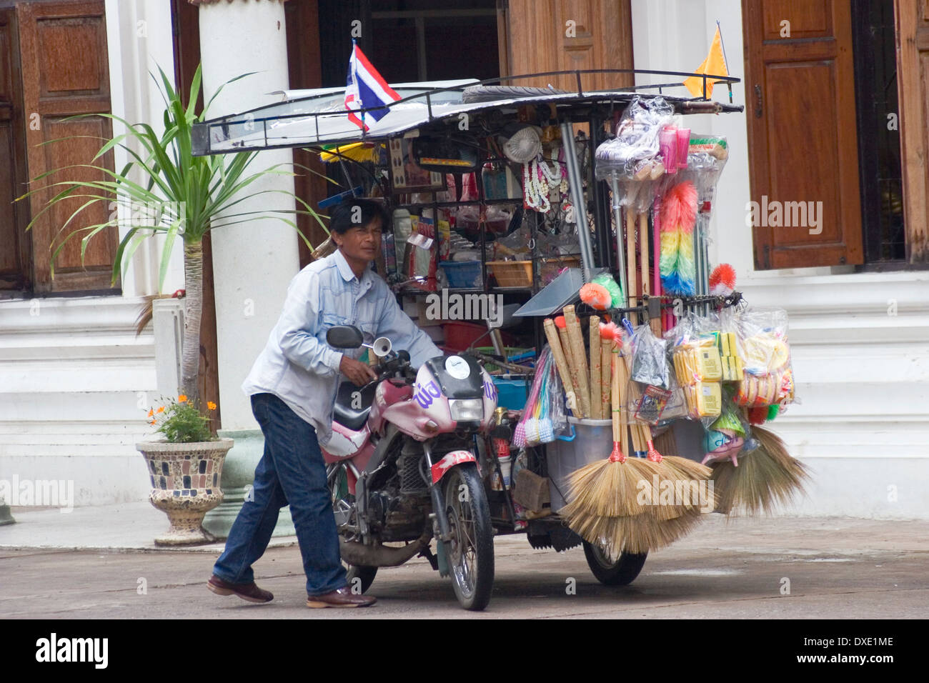 A man is pushing a motorcycle with a sidecar filled with household supplies on a city street in Khorat, Thailand. Stock Photo
