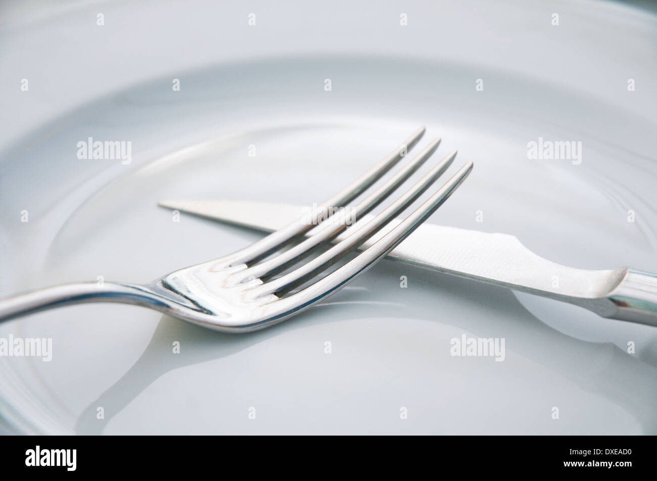 Fork and knife crossing on an empty plate. Close view. Stock Photo