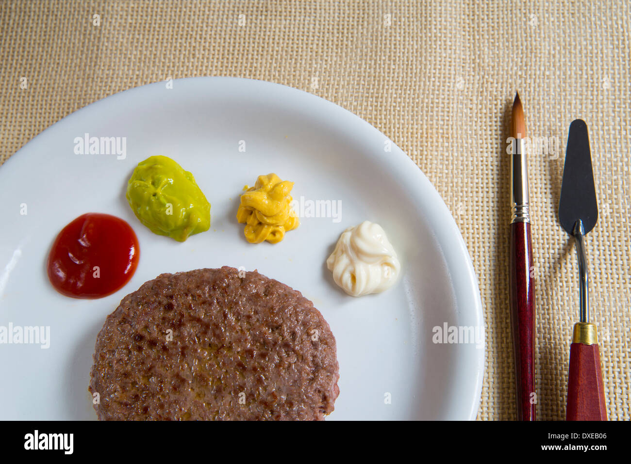 Artistic cuisine: hamburger and palette of assorted sauces, served with paint brush and palette knife as fork and knife. Stock Photo