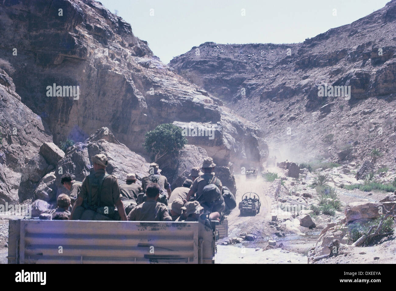 British soldiers driving in army trucks along a graded road through a wadi in the desert during the Aden Emergency, 1967 Stock Photo