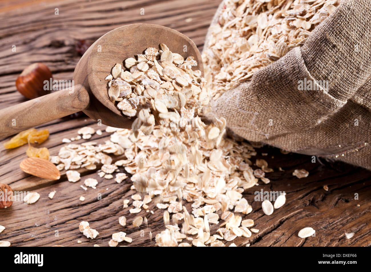 Rolled oats in the wooden spoon and sack on old wooden table. Stock Photo