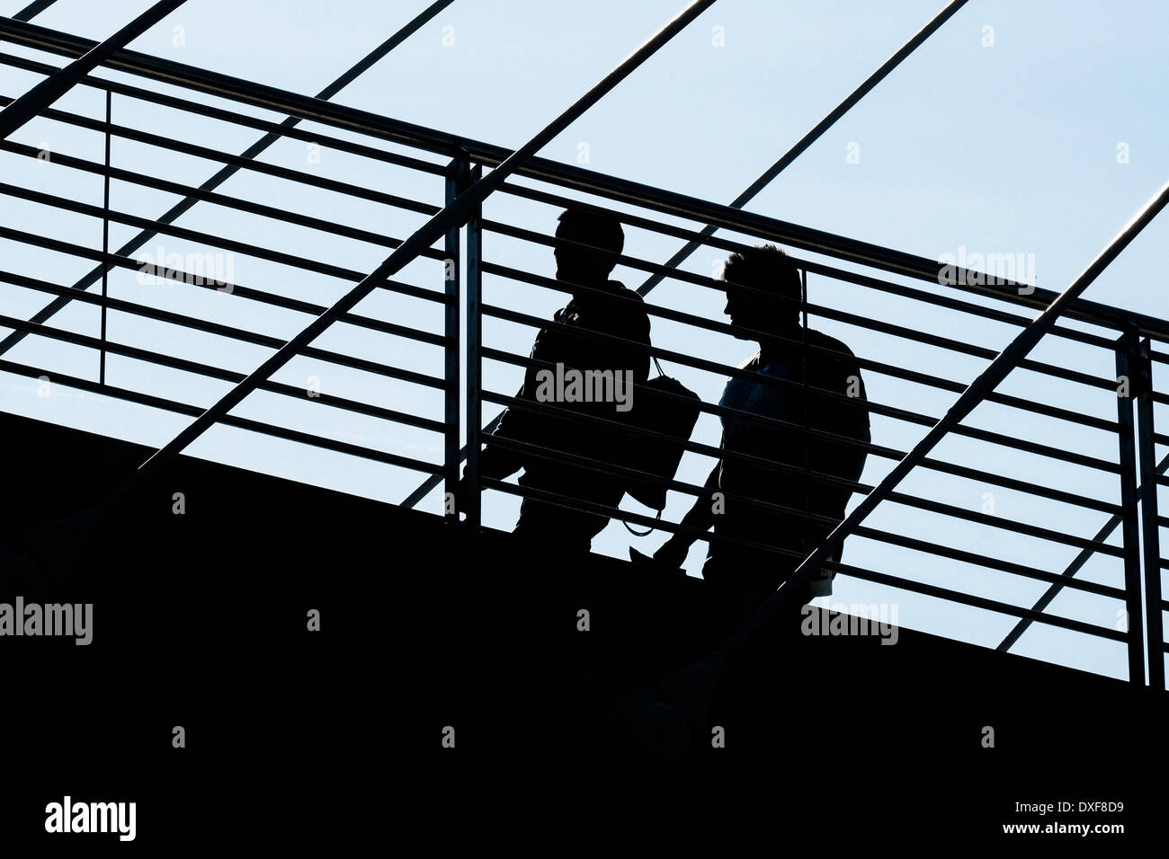 The silhouette of two people walking across a bridge. Stock Photo