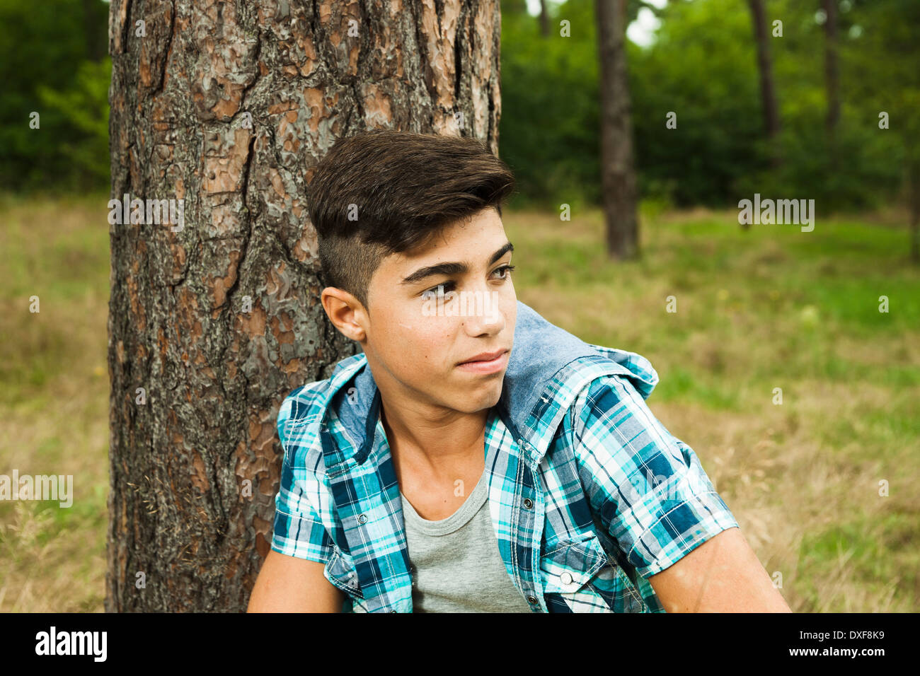 Close-up portrait of boy sitting beside tree in park, Germany Stock Photo