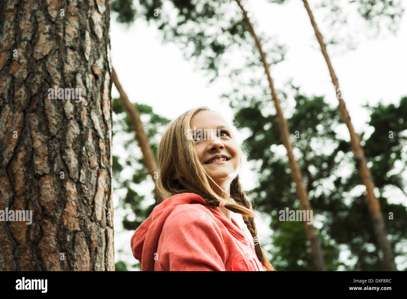 Portrait of girl standing next to tree in park, looking upward, Germany Stock Photo