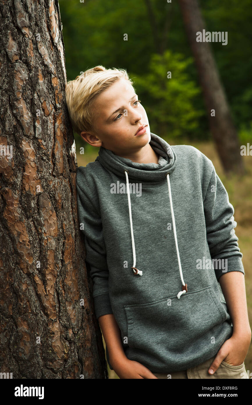 Portrait of boy standing in front of tree in park, looking into the distance, Germany Stock Photo