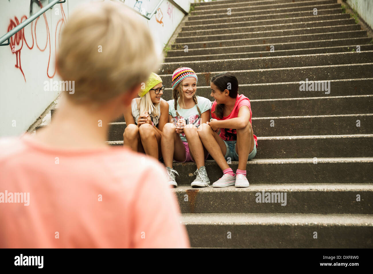 Backview of boy watching girls sitting on stairs outdoors, Germany Stock Photo