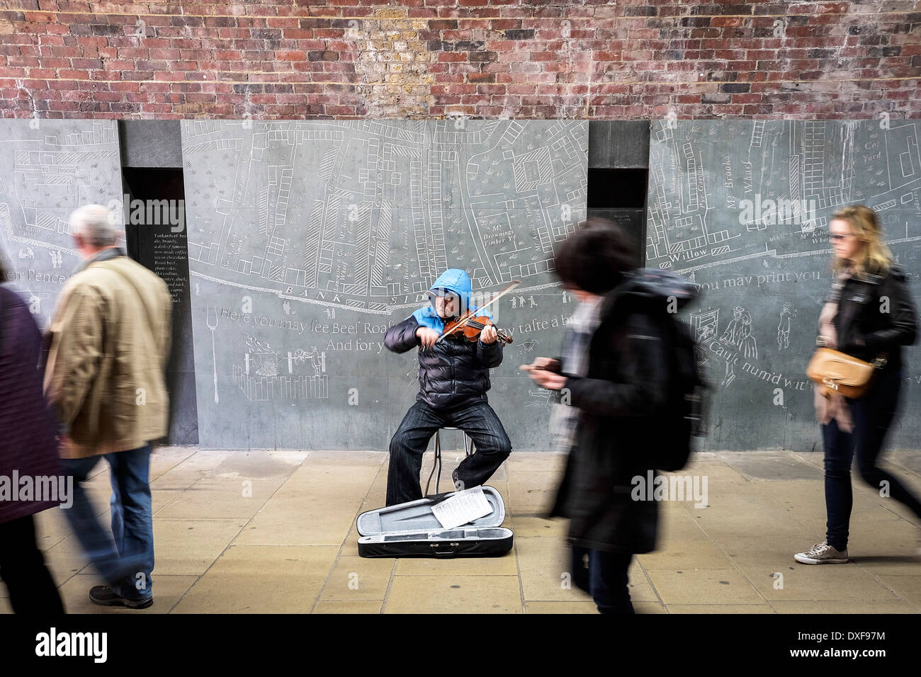 A busker playing a violin as people walk past. Stock Photo