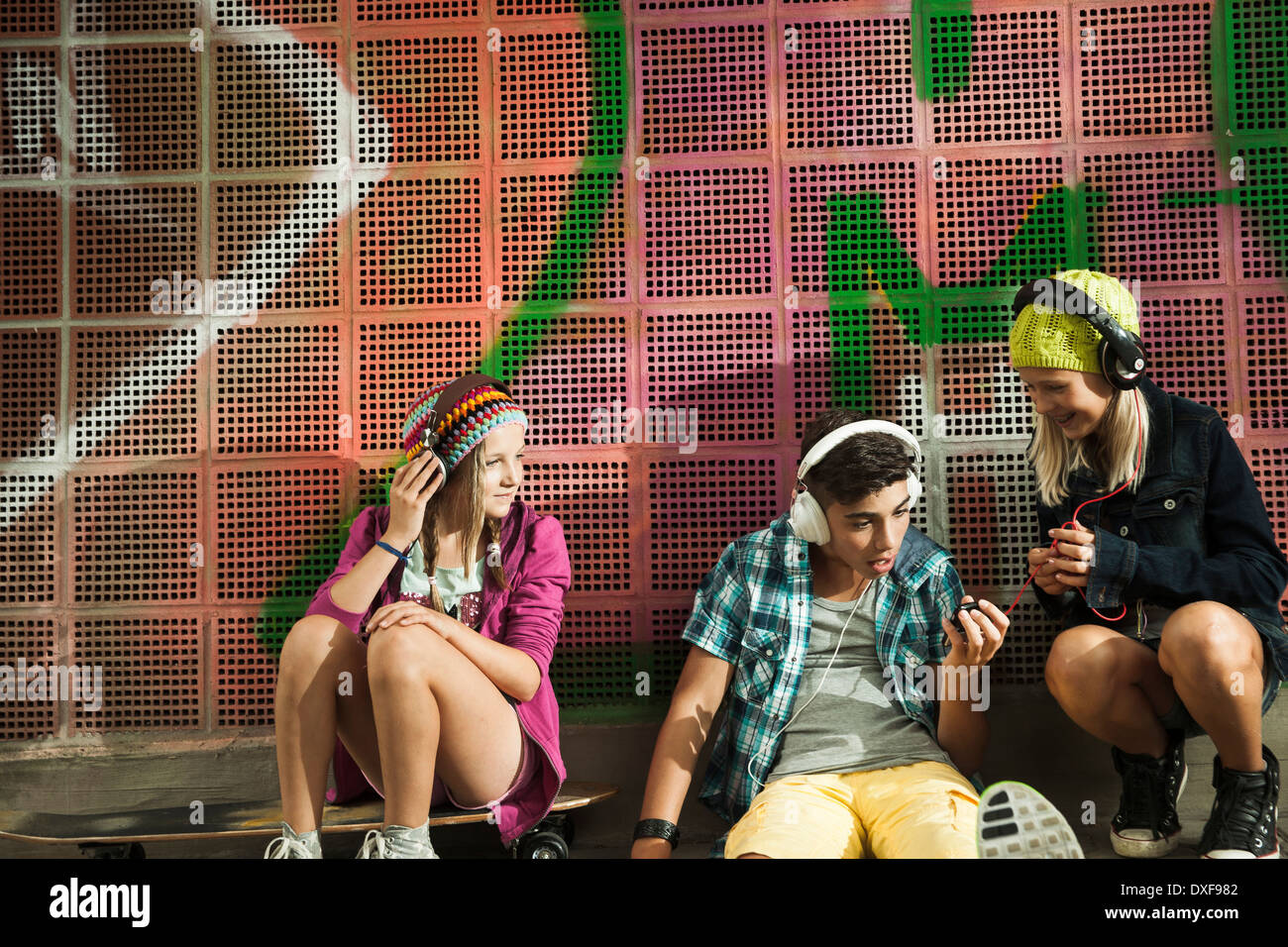 Children sitting next to wall outdoors, wearing headphones and listening to music, Germany Stock Photo
