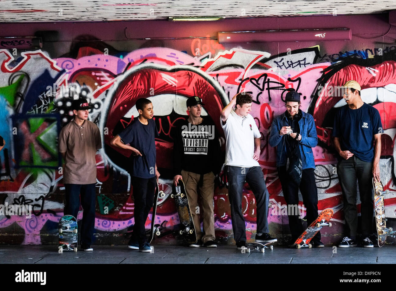 Young skateboarders standing against a grafitti covered wall at the South Bank Skateboard Park in London. Stock Photo