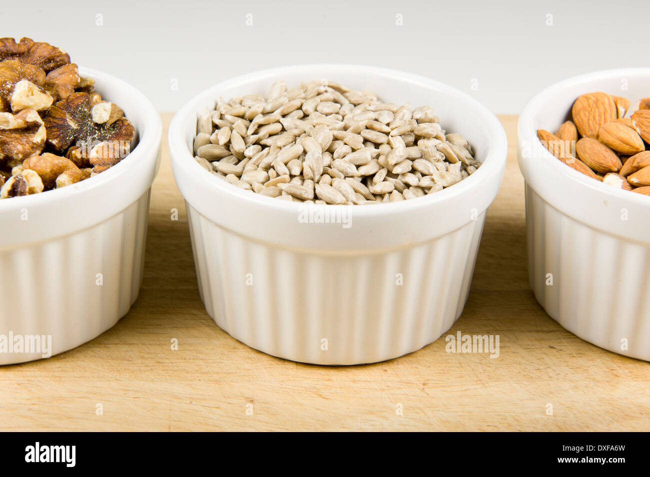 Close up photograph of three white ramekin bowls individually filled with walnuts, sunflower seed, and almonds. Stock Photo