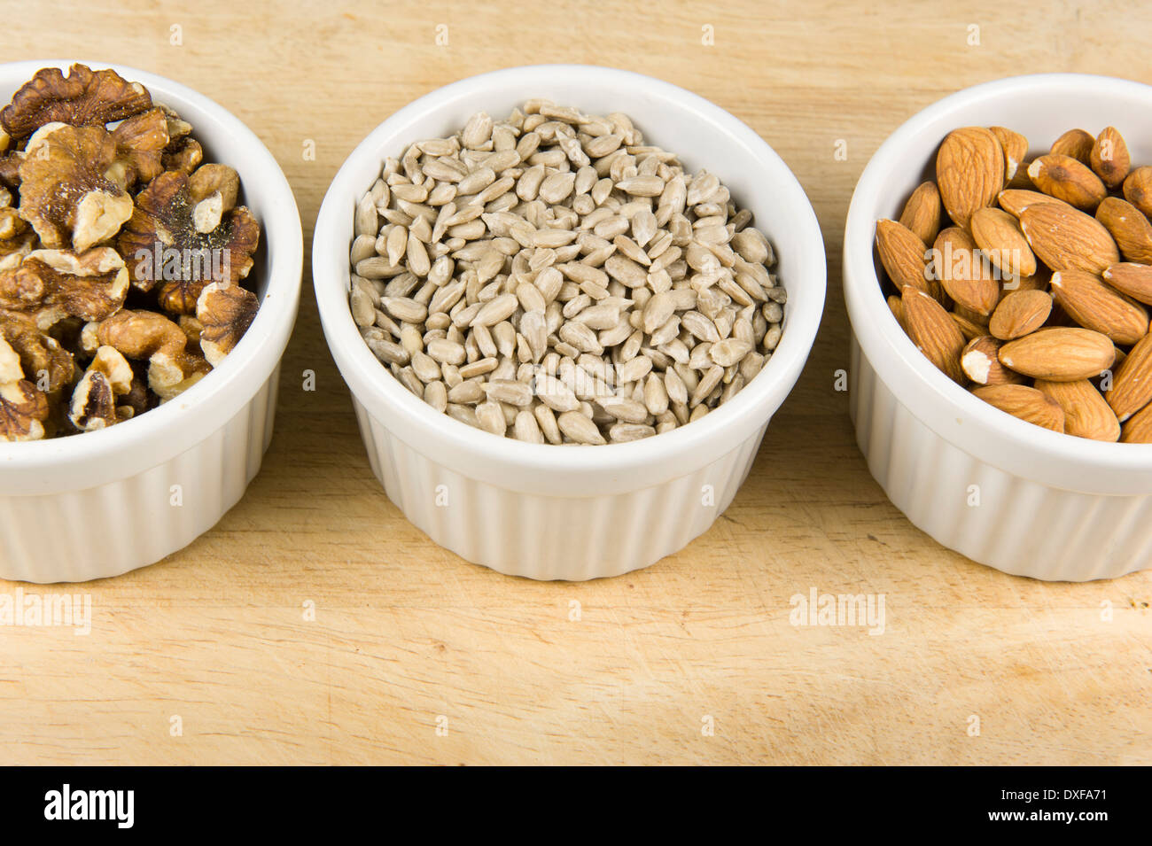 Close up photograph of three white ramekin bowls individually filled with walnuts, sunflower seed, and almonds. Stock Photo