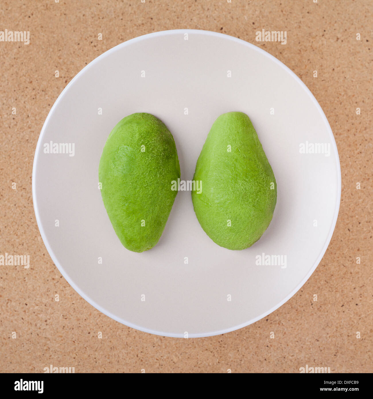 Fresh peeled halved avocado on plate, over wooden background. Stock Photo