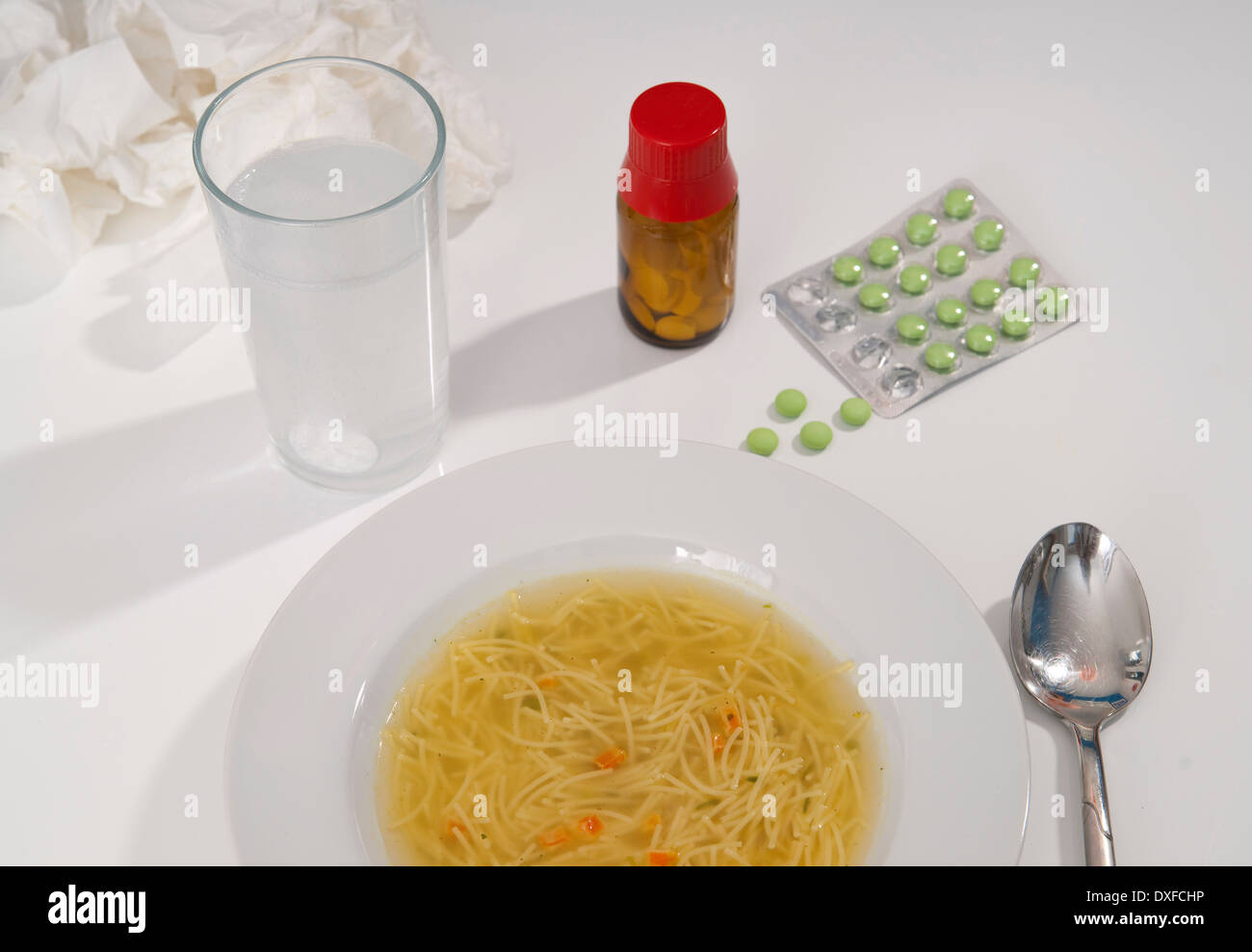 Medications, bowl of chicken soup and glass of water on table, studio shot Stock Photo