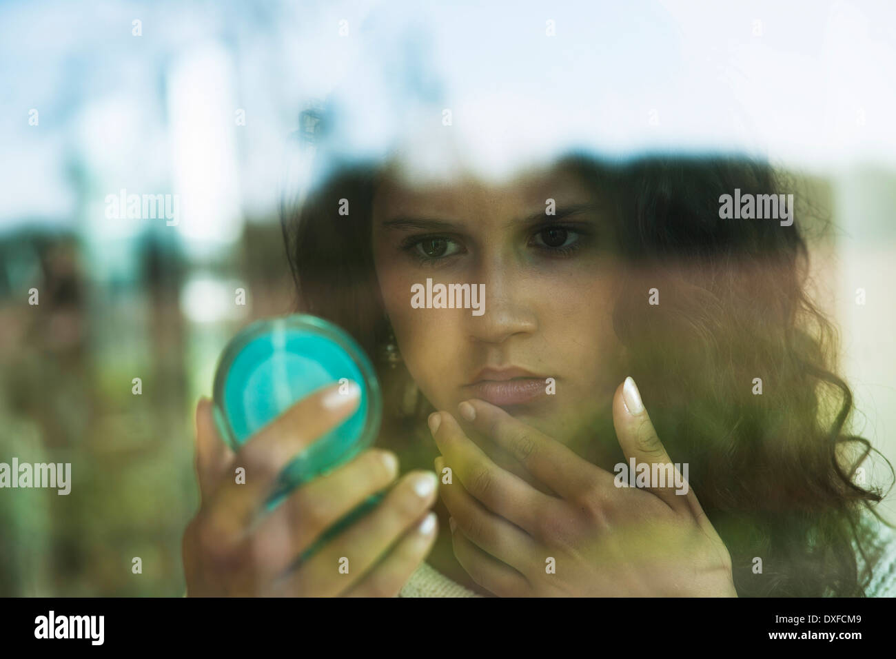 Close-up portrait of teenage girl looking in mirror in compact, in front of window, Germany Stock Photo