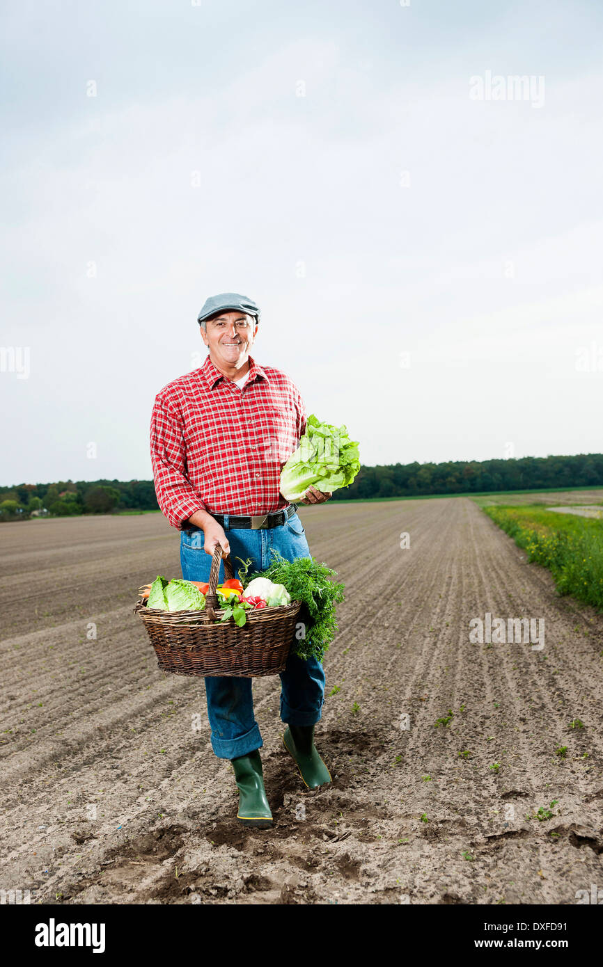 Farmer standing in field with basket of fresh vegetables, smiling and looking at camera, Hesse, Germany Stock Photo