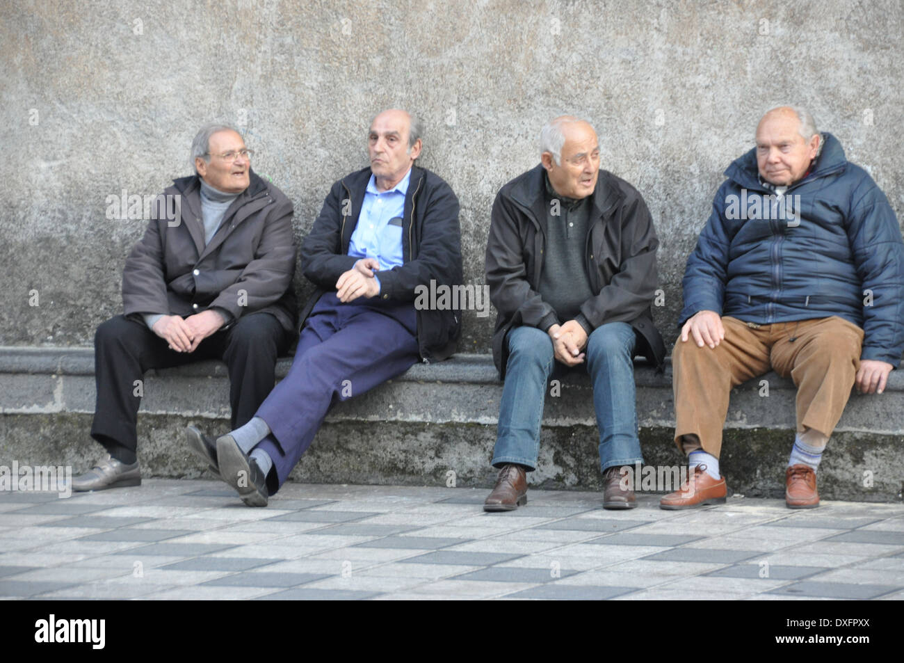 Four elderly men sitting on a bench chatting and passing the time of day. Stock Photo