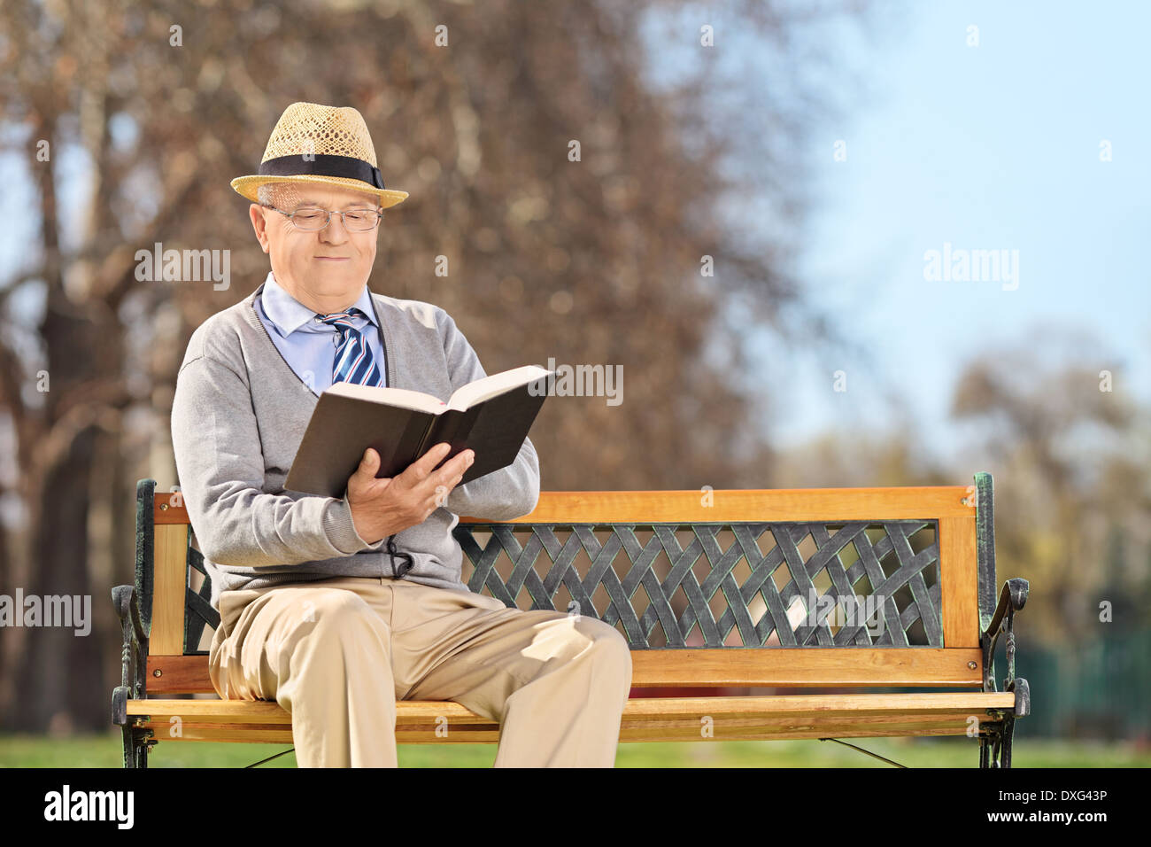 Senior relaxing with a book seated on bench outdoors Stock Photo