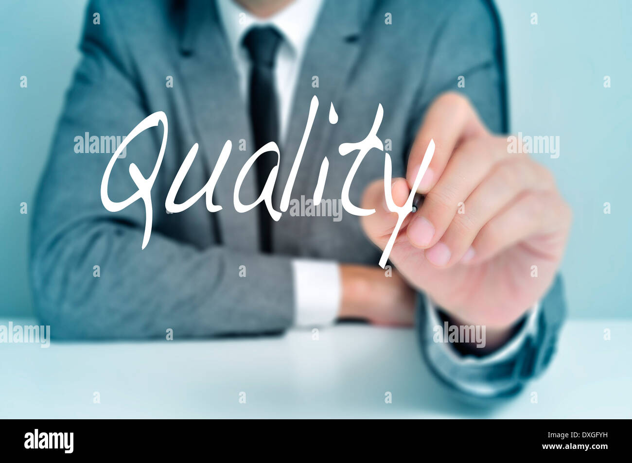 businessman sitting in a desk writing the word quality in the foreground Stock Photo