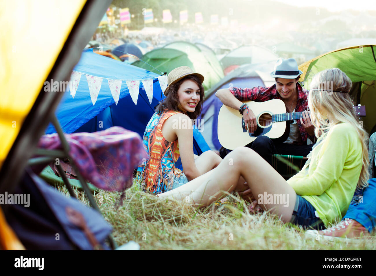 Friends with guitar hanging out near tents at music festival Stock Photo