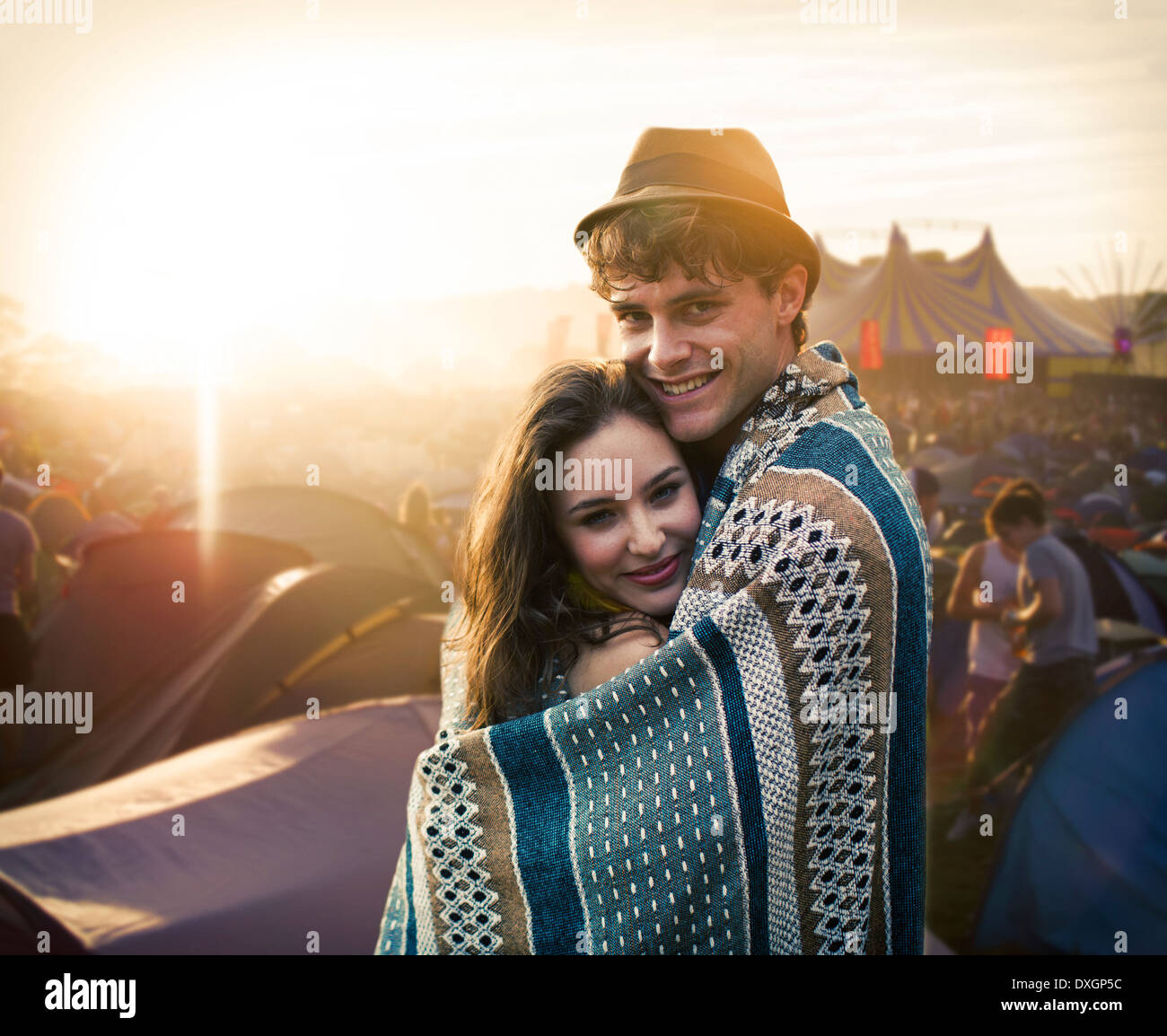 Couple wrapped in a blanket outside tents at music festival Stock Photo