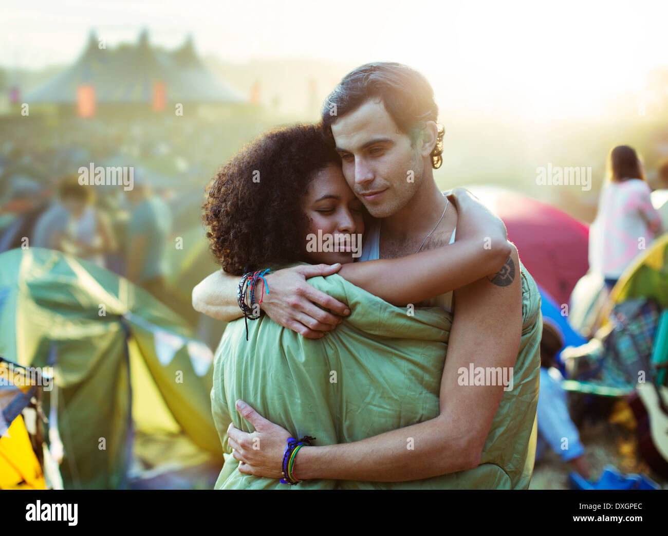 Couple in sleeping bag hugging outside tents at music festival Stock Photo