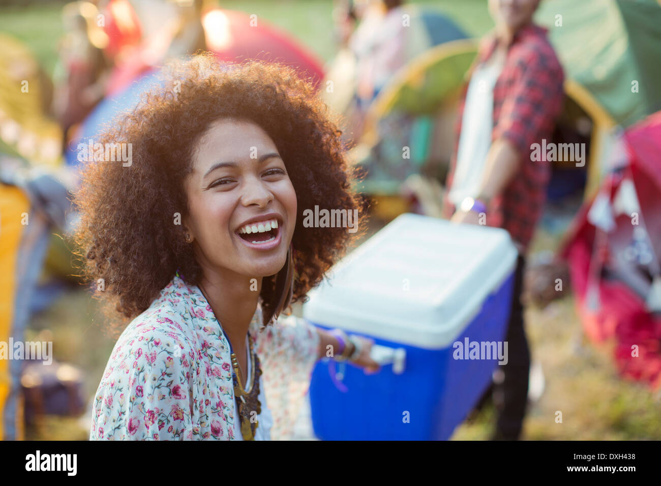 Portrait of laughing woman helping man carry cooler outside tents at music festival Stock Photo