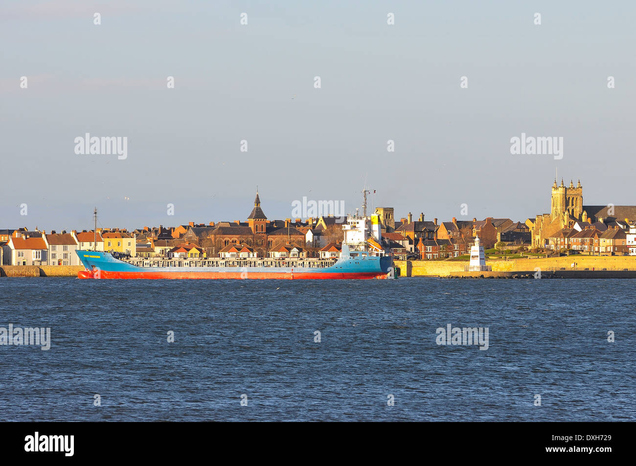 A large blue and red ship passes closes to houses and a church on the historic Headland of Hartlepool in north east England, UK. Stock Photo