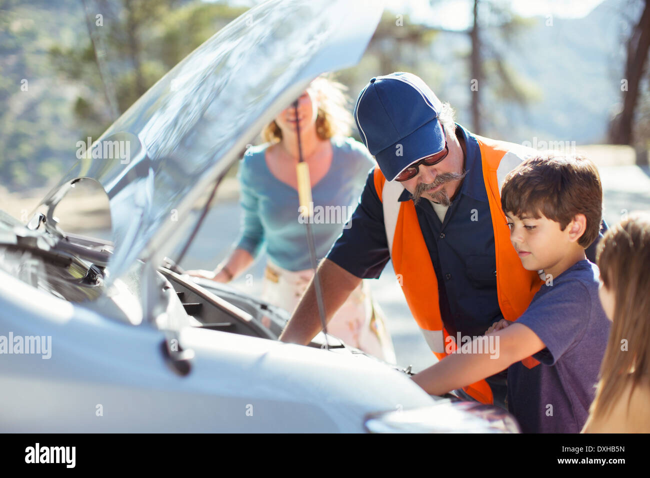 Boy watching roadside mechanic check car engine Stock Photo