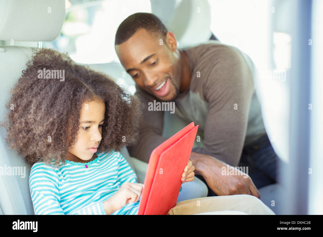 Father and daughter using digital tablet in back seat of car Stock Photo