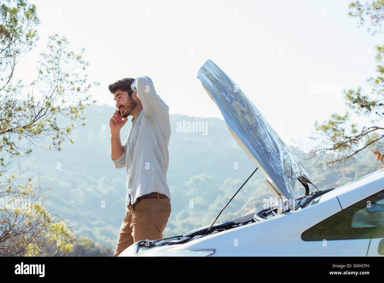 Man talking on cell phone with automobile hood raised at roadside Stock Photo