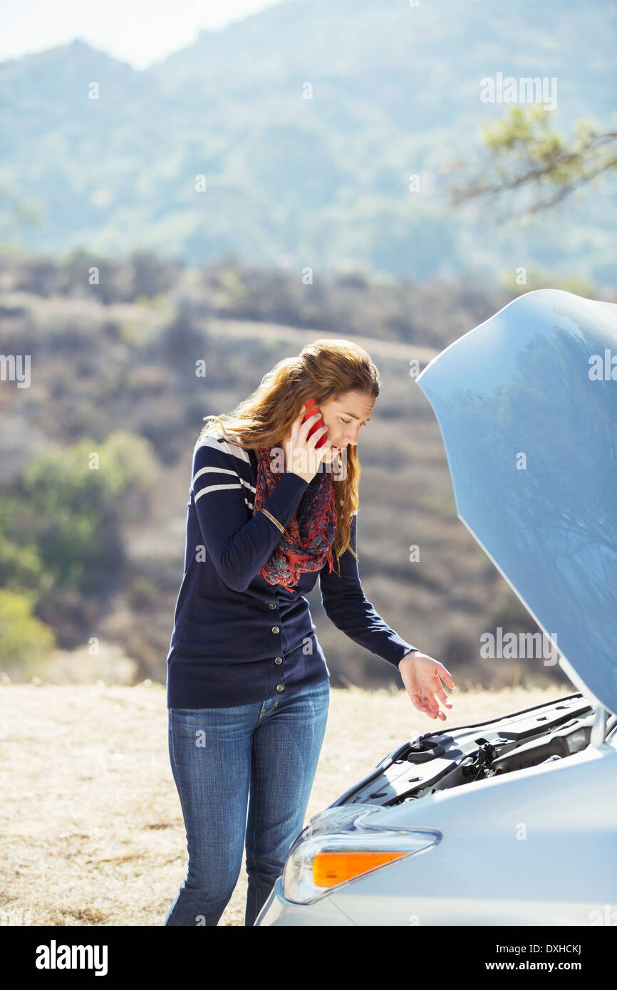 Woman talking on cell phone with automobile hood raised at roadside Stock Photo