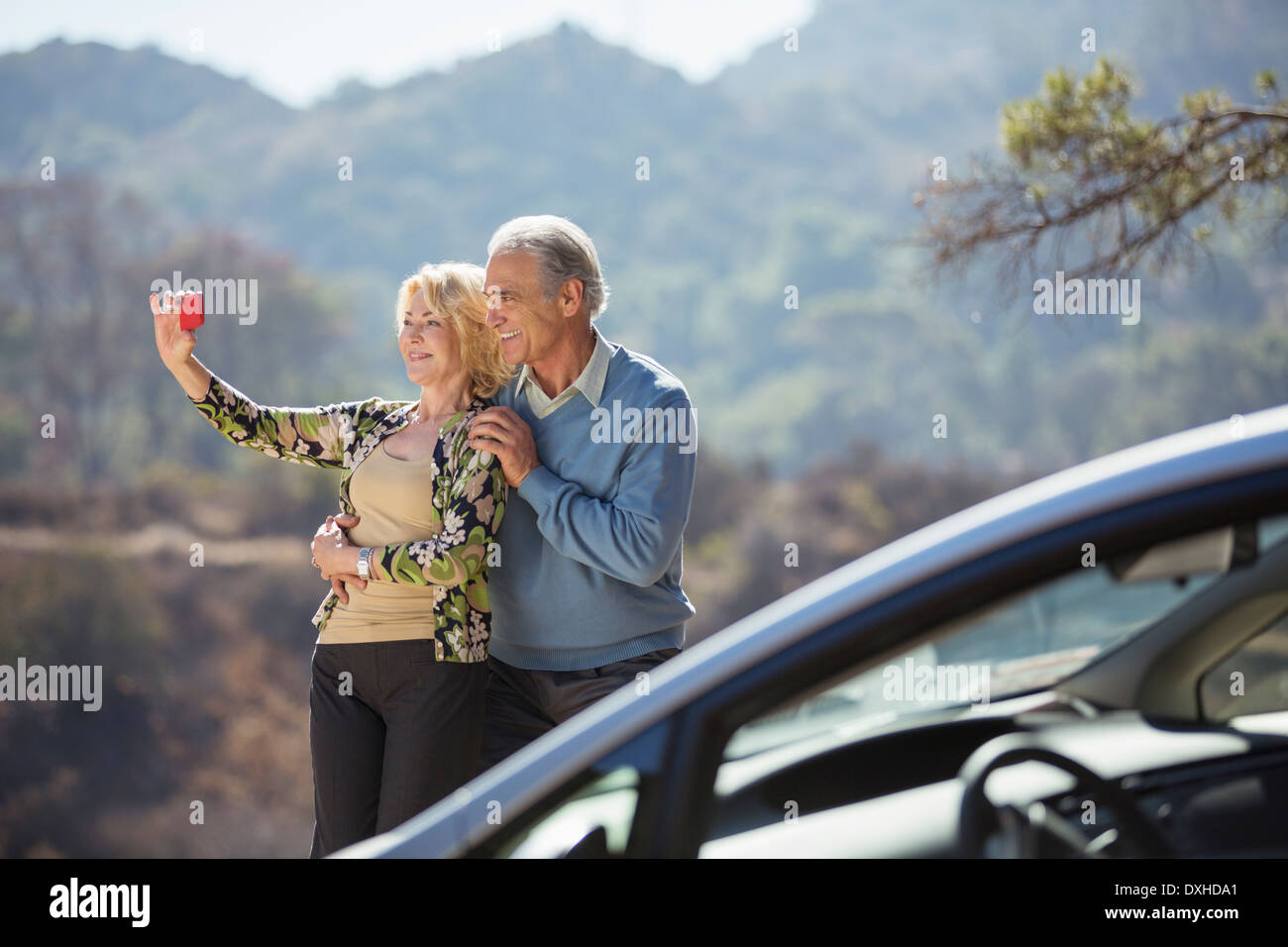 Senior couple taking self-portrait at roadside outside car Stock Photo
