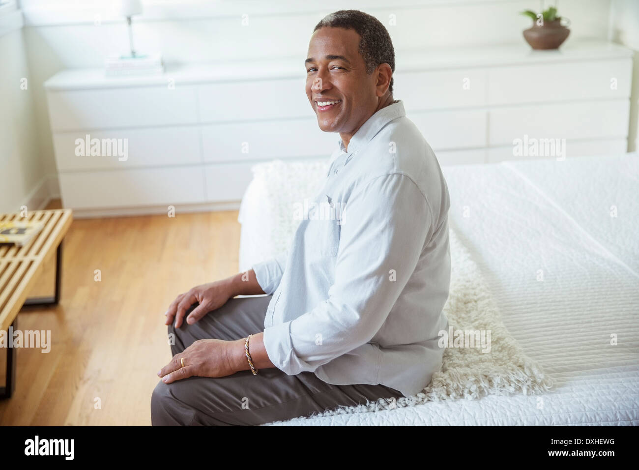 Portrait of smiling senior man sitting at the edge of bed Stock Photo