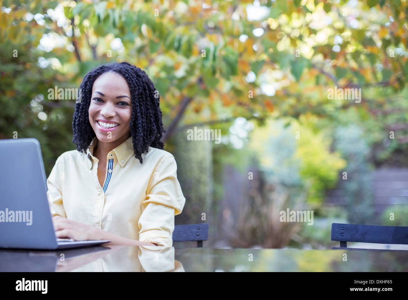 Portrait of smiling woman using laptop at patio table Stock Photo