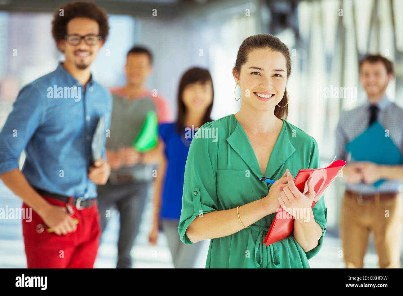Portrait of creative businesswoman with folder and co-workers in corridor Stock Photo