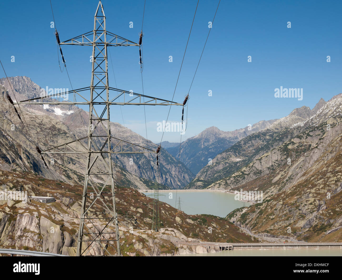 High voltage electric power line in the Swiss alps in front of the lake Grimsel reservoir, dam and utilites. Stock Photo