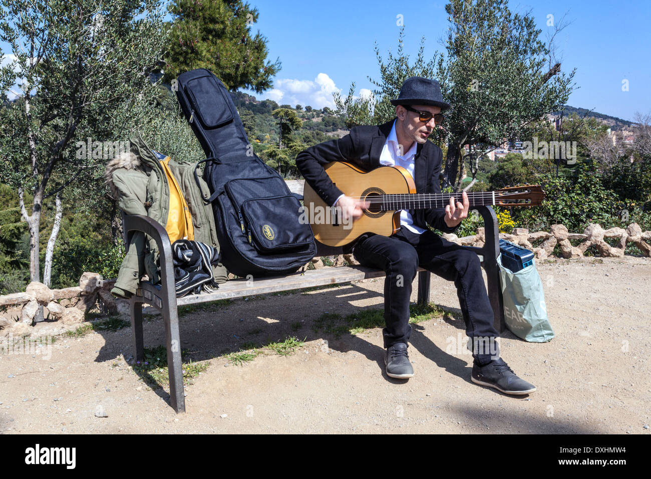 A male busker seated on a bench, playing a Spanish guitar, Park Güell, Barcelona, Spain. Stock Photo