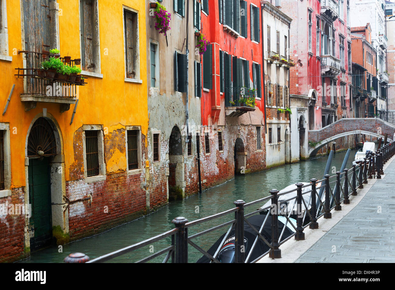 Iron railing on walkway next to canal with red and yellow buildings in ...