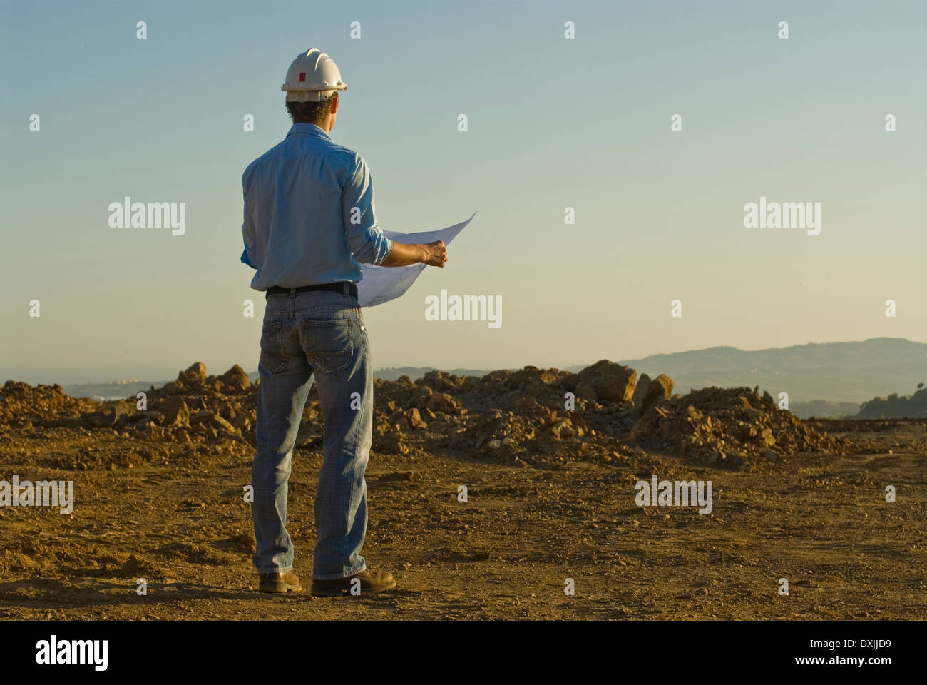 Young engineer with plan on construction site rear view Stock Photo
