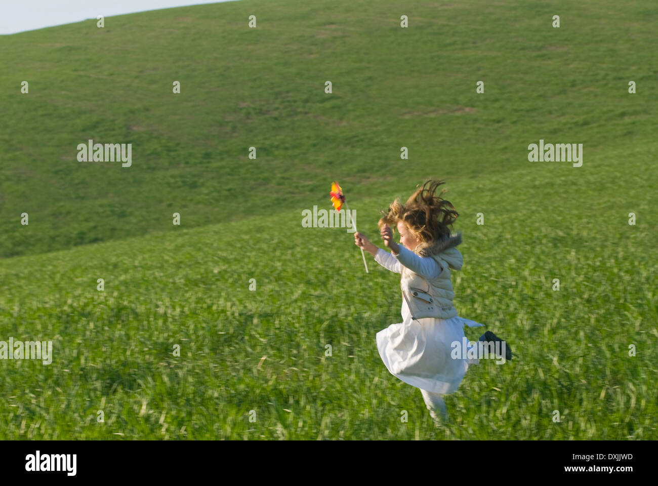 young girl with wind wheel running in green fields Stock Photo