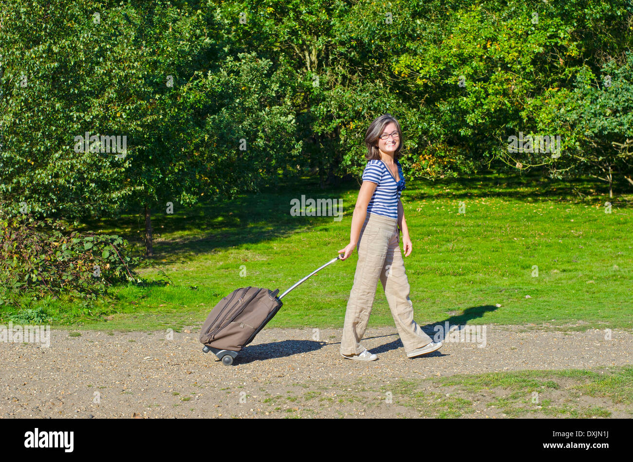 woman walking though park pulling roller case Stock Photo