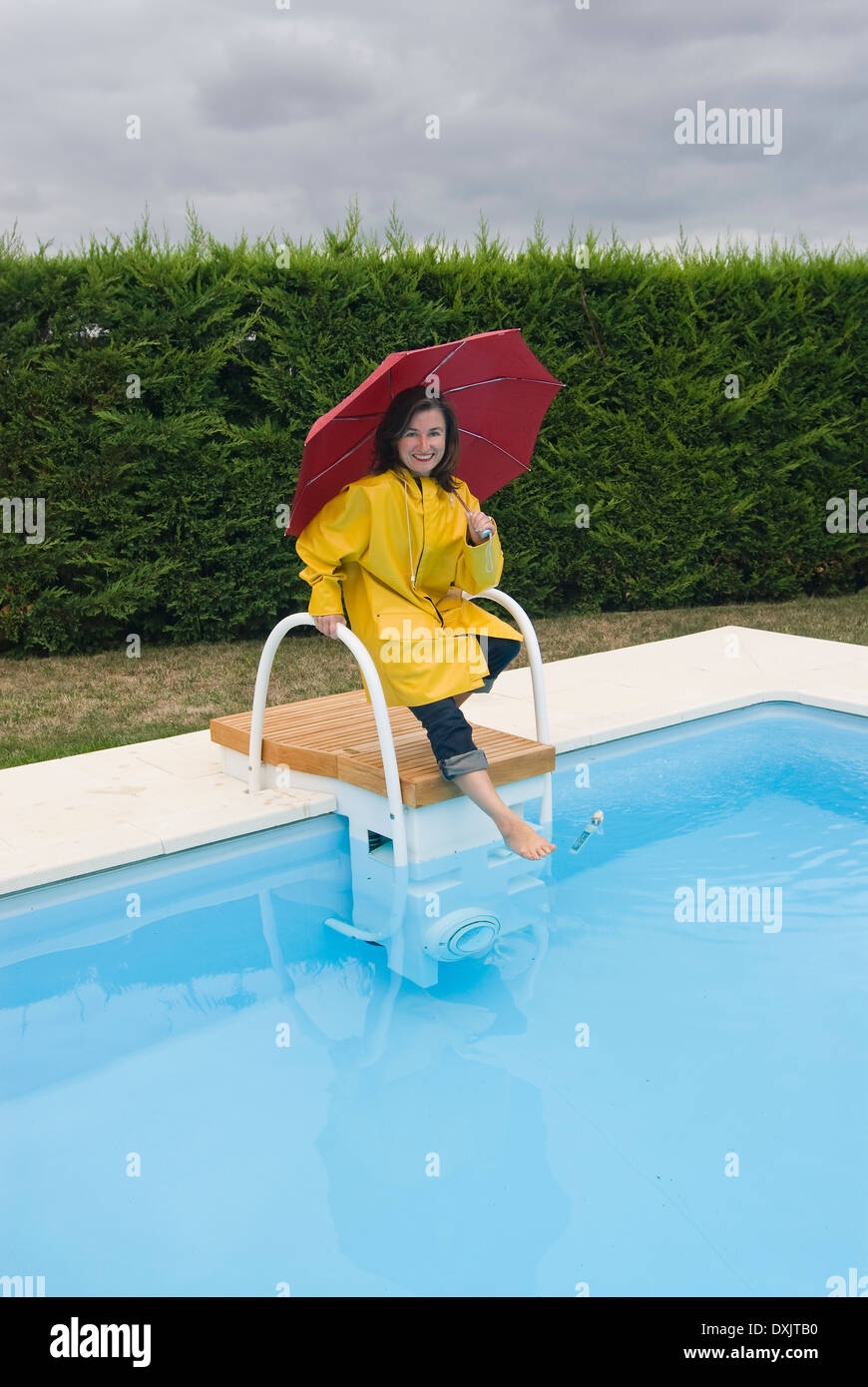 woman in rainwear tipping toe into swimming pool Stock Photo
