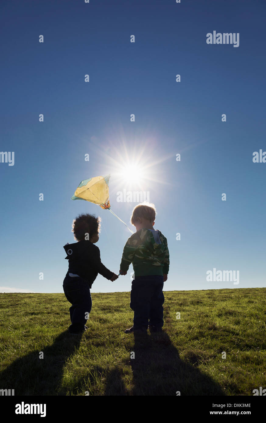 Boys watching kite flying against blue sky Stock Photo