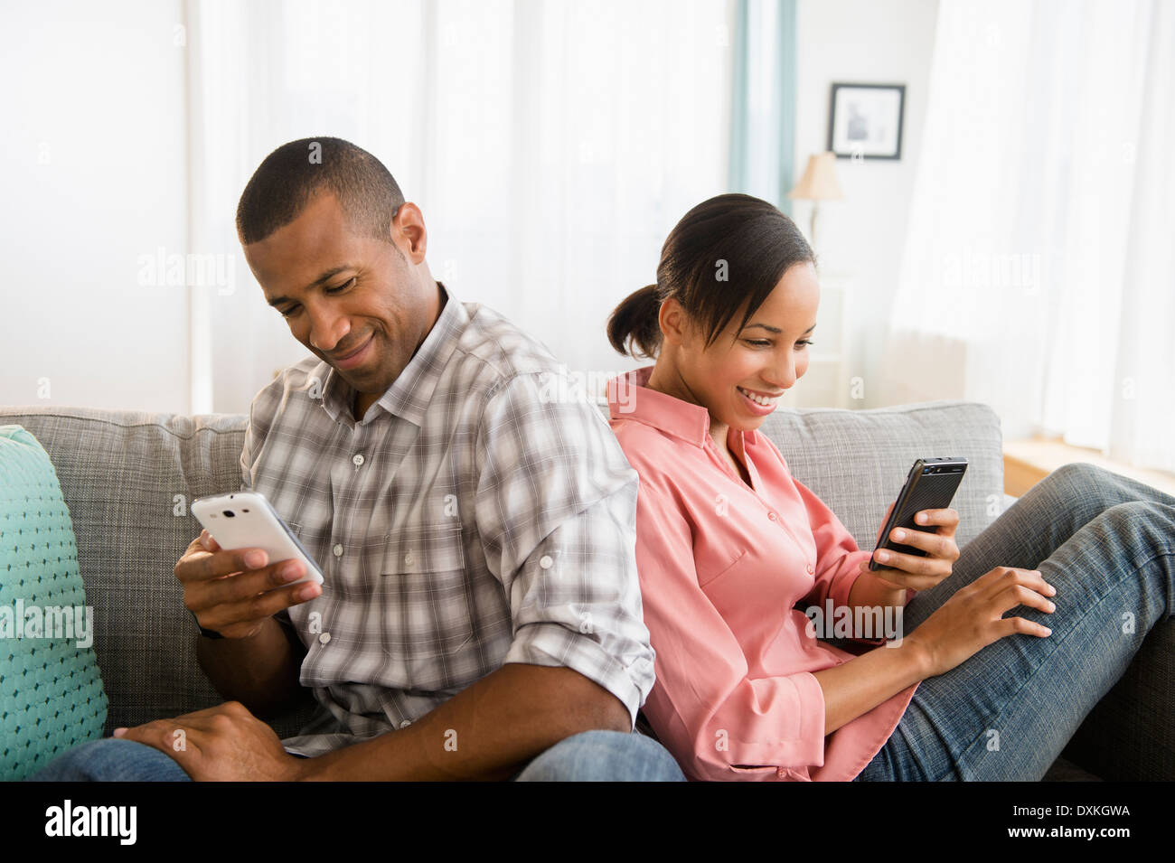 Couple using cell phones back to back on sofa Stock Photo